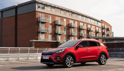 A red Kia Niro is parked on the top open floor of a multi-storey car park.